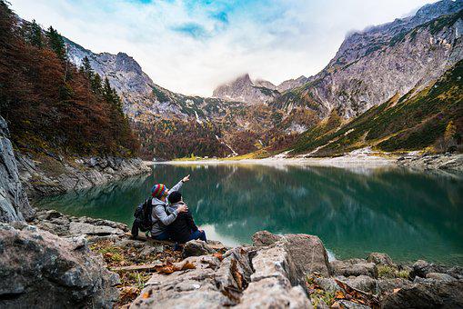 Dwójka ludzi siedzących nad brzegiem górskiego jeziora