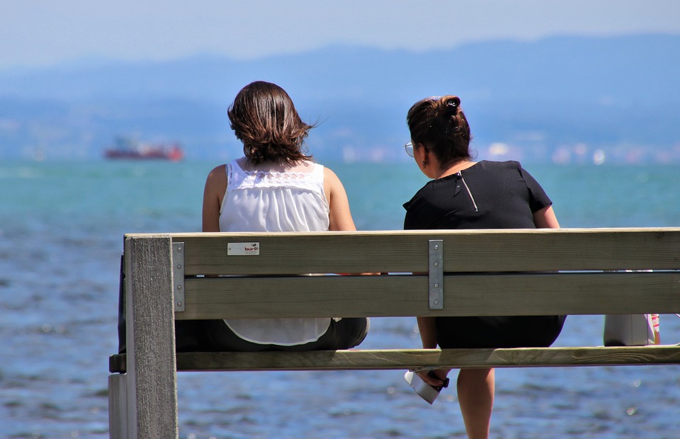 dwie kobiety siedzące na ławce nad morzem