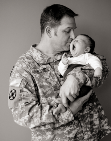 mężczyzna w mundurze tulący do twarzy niemowlaka