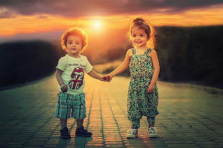 mały chłopiec i dziewczynka trzymający się za ręce na tle zachodu słońca