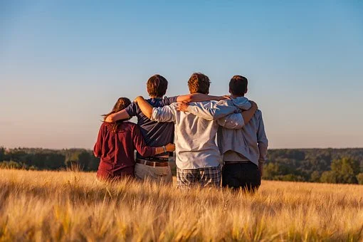czworo nastolatków obejmujących się w rzędzie stojących w wysokiej trawie