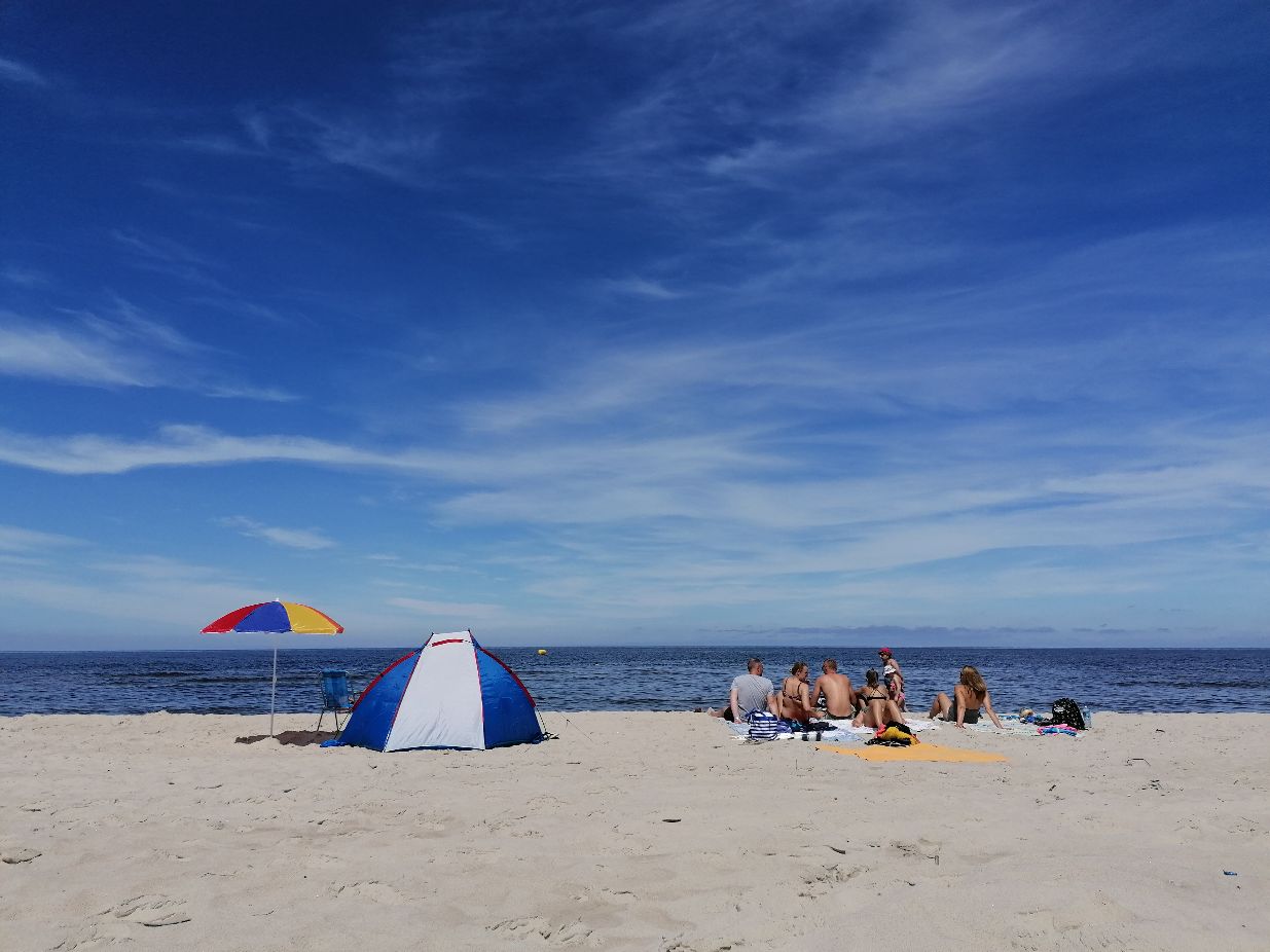 kilka osób siedzących na plaży obok namiotu i parasola