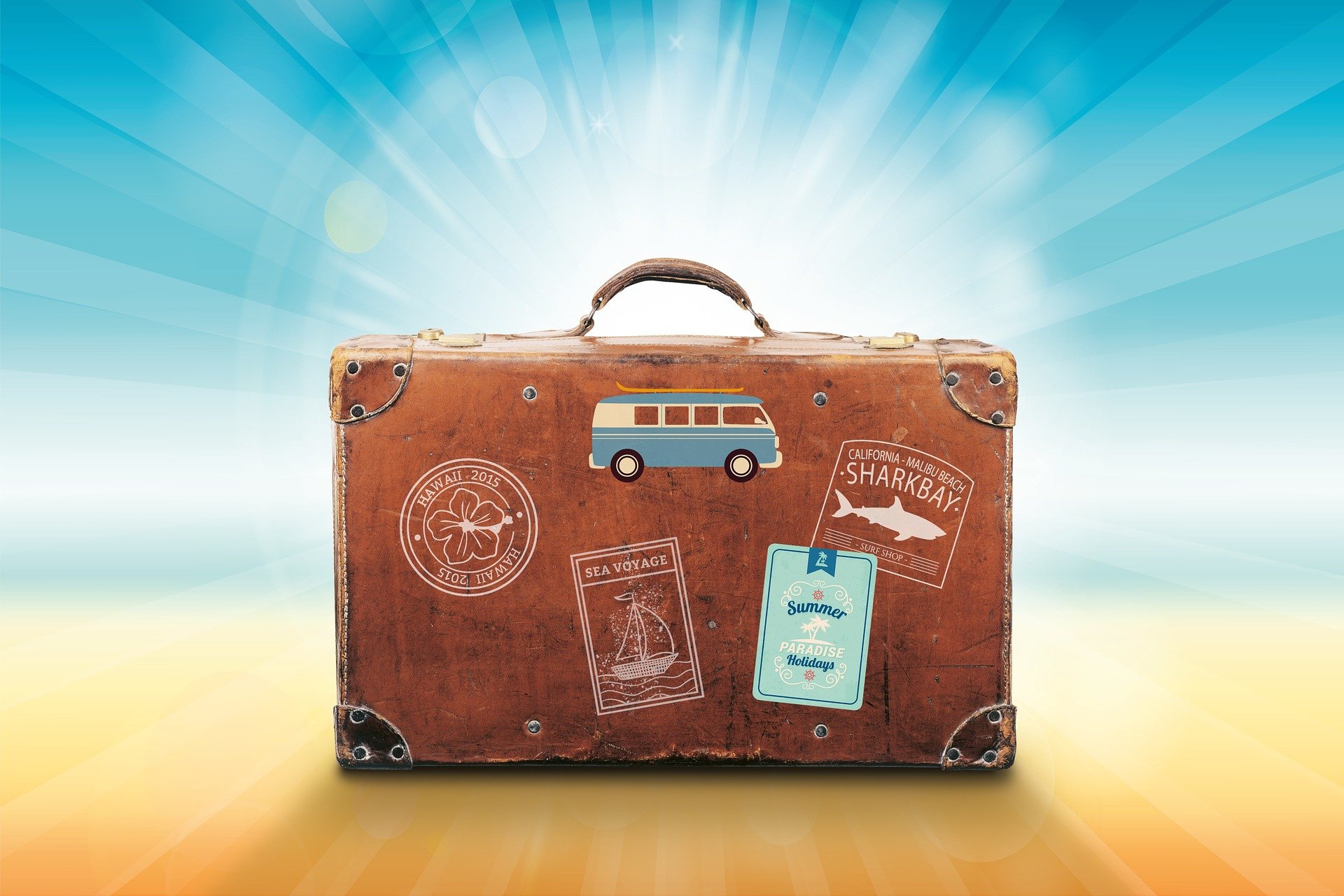 walizka podróżna z naklejkami stojąca na plaży