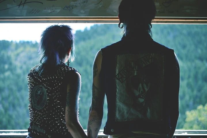 para młodych ludzi ubranych w stylu punk patrzy przez okno trzymając się za ręce