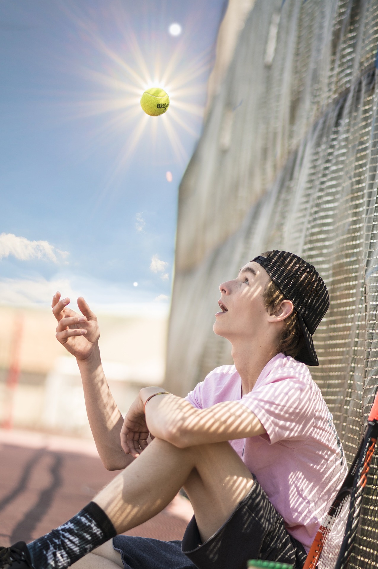 siedzący chłopiec podrzucający piłkę do tenisa