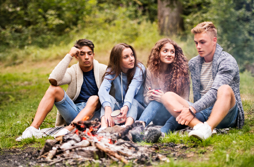 Czworo nastolatków siedzących przy ognisku w lesie