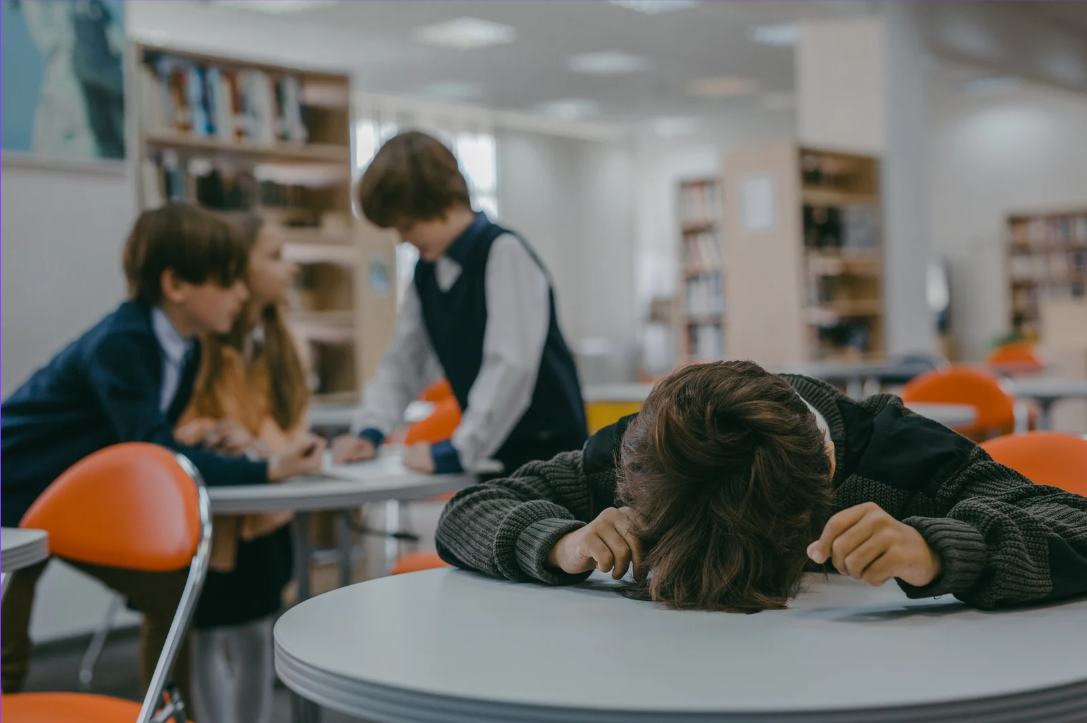 sala lekcyjna w tle a na pierwszym planie uczeń z głową położoną na biurku